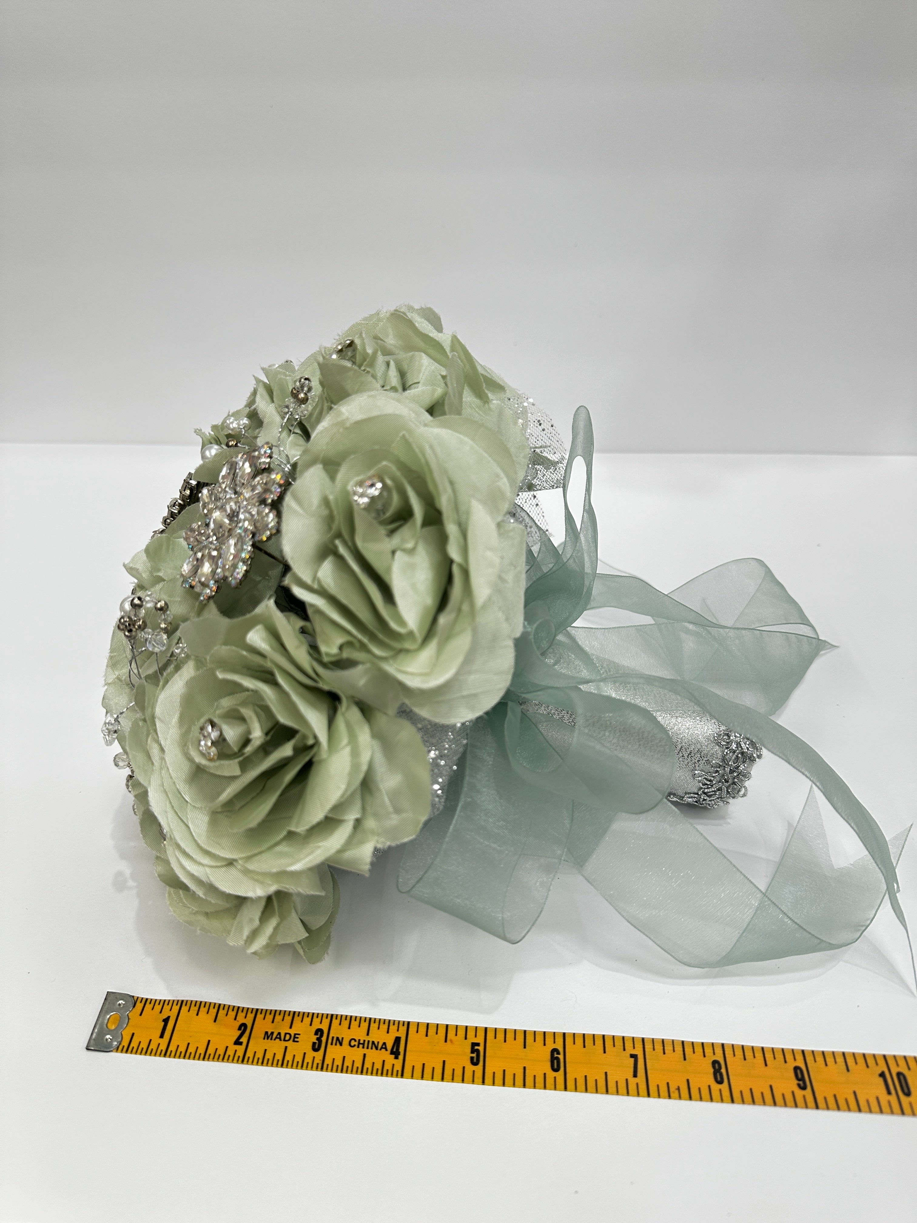 sage Green floral arrangement with decorative elements on a white background, measured against a ruler.