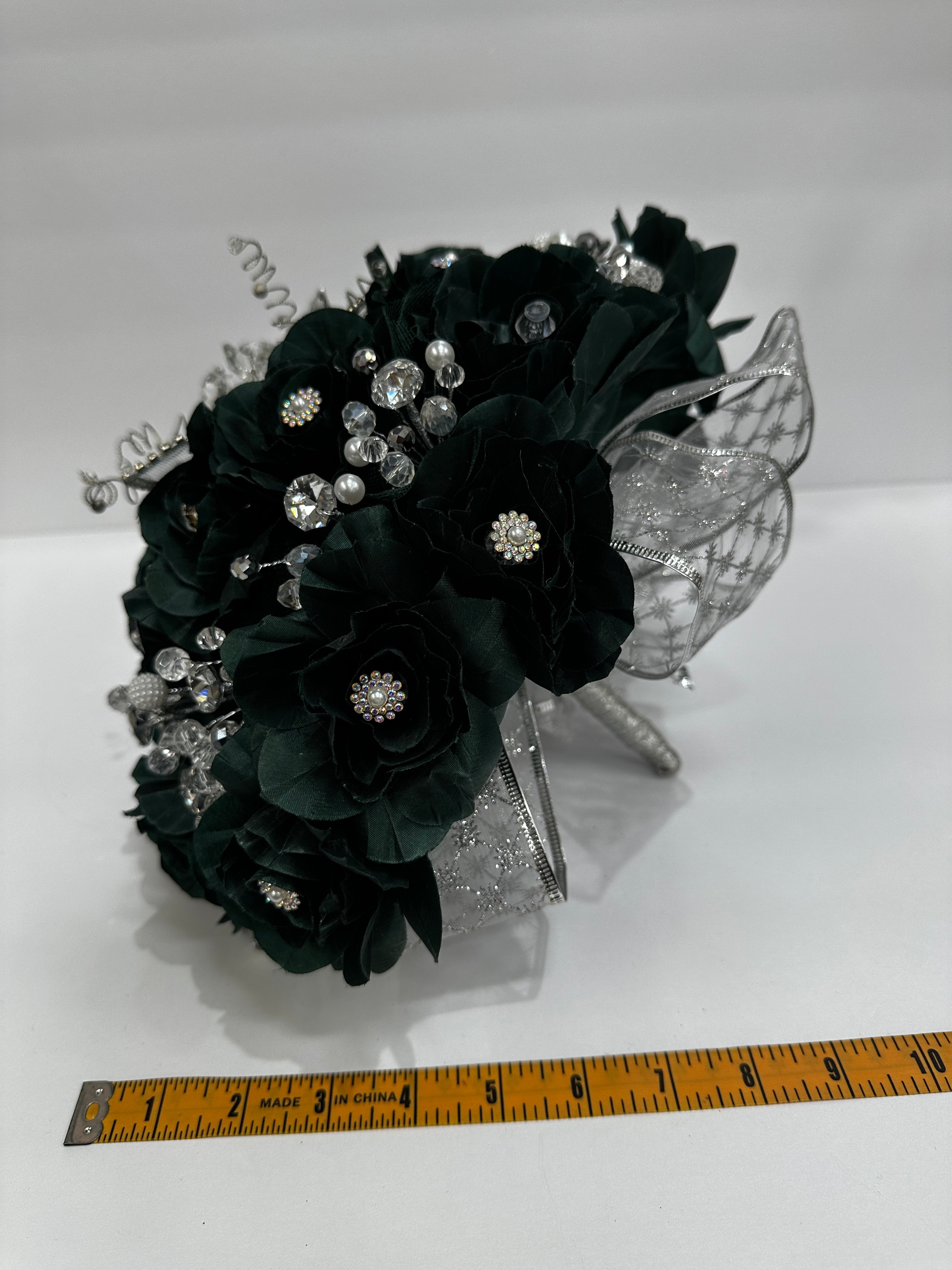 dark green bouquet with silver accents next to a ruler on a white background