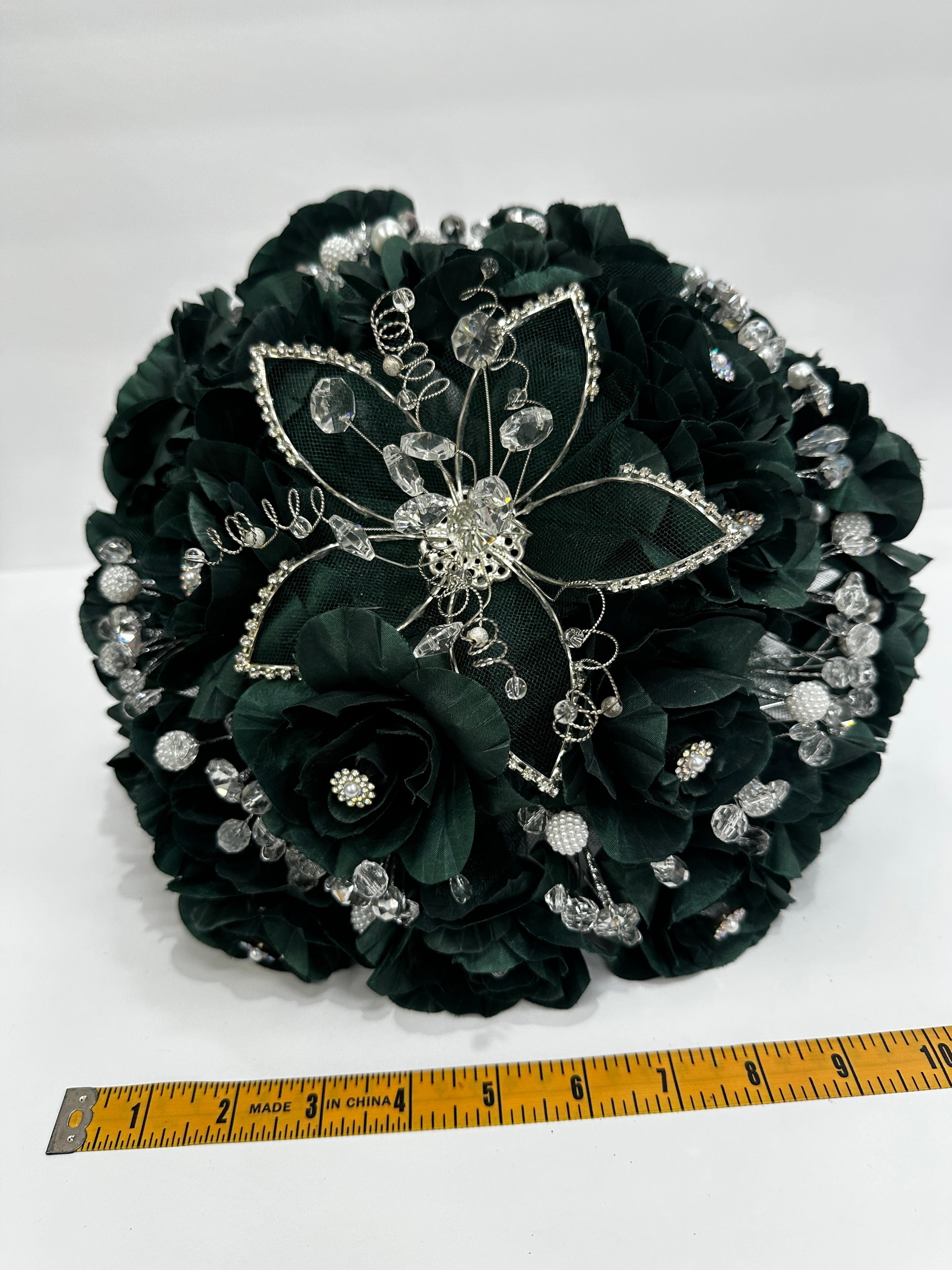 Decorative dark green bouquet  with embellishments on a white background, measured by a ruler about 10 inches across
