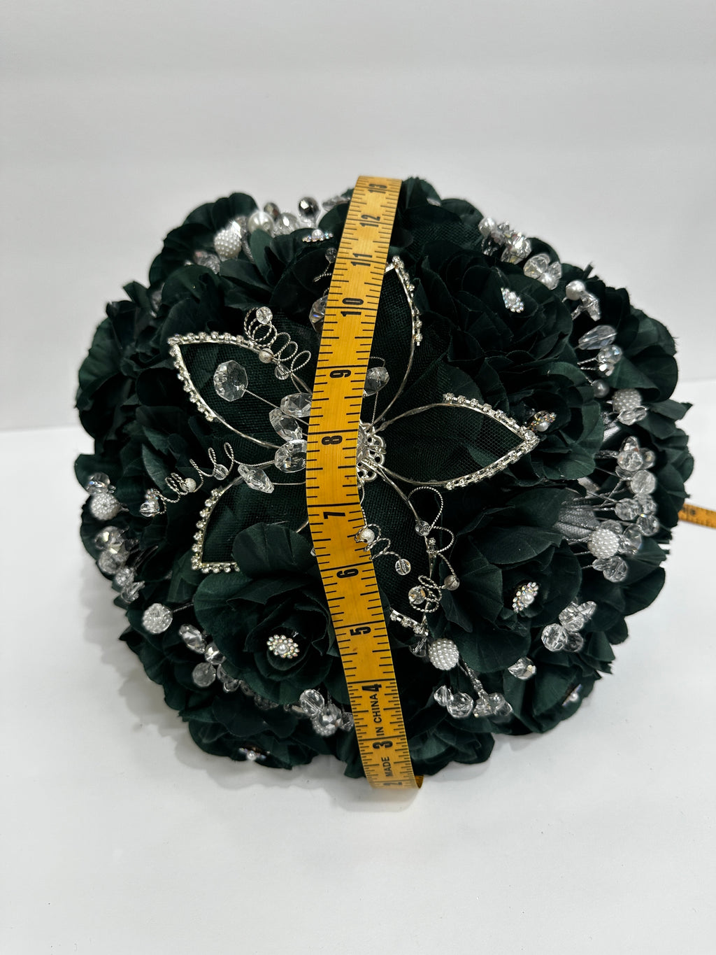 dark green bouquet with decorative elements and a measuring tape for scale measuring hemeisphere about 14 inches on a white background
