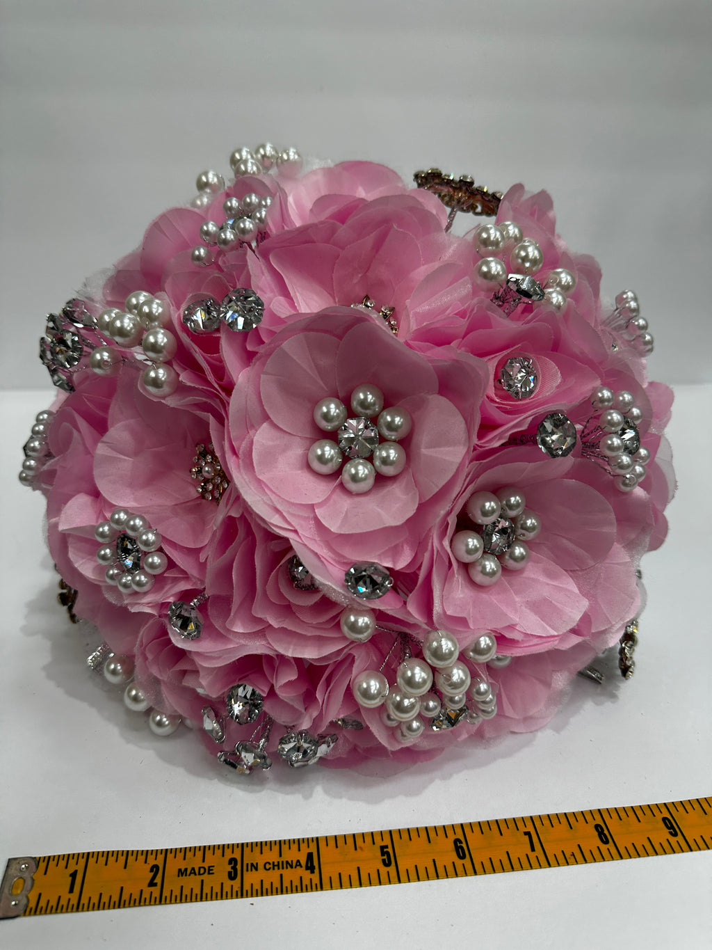 Pink floral bouquet with decorative silver application  and pearls on a white background with a ruler for scale about 9 inches length.
