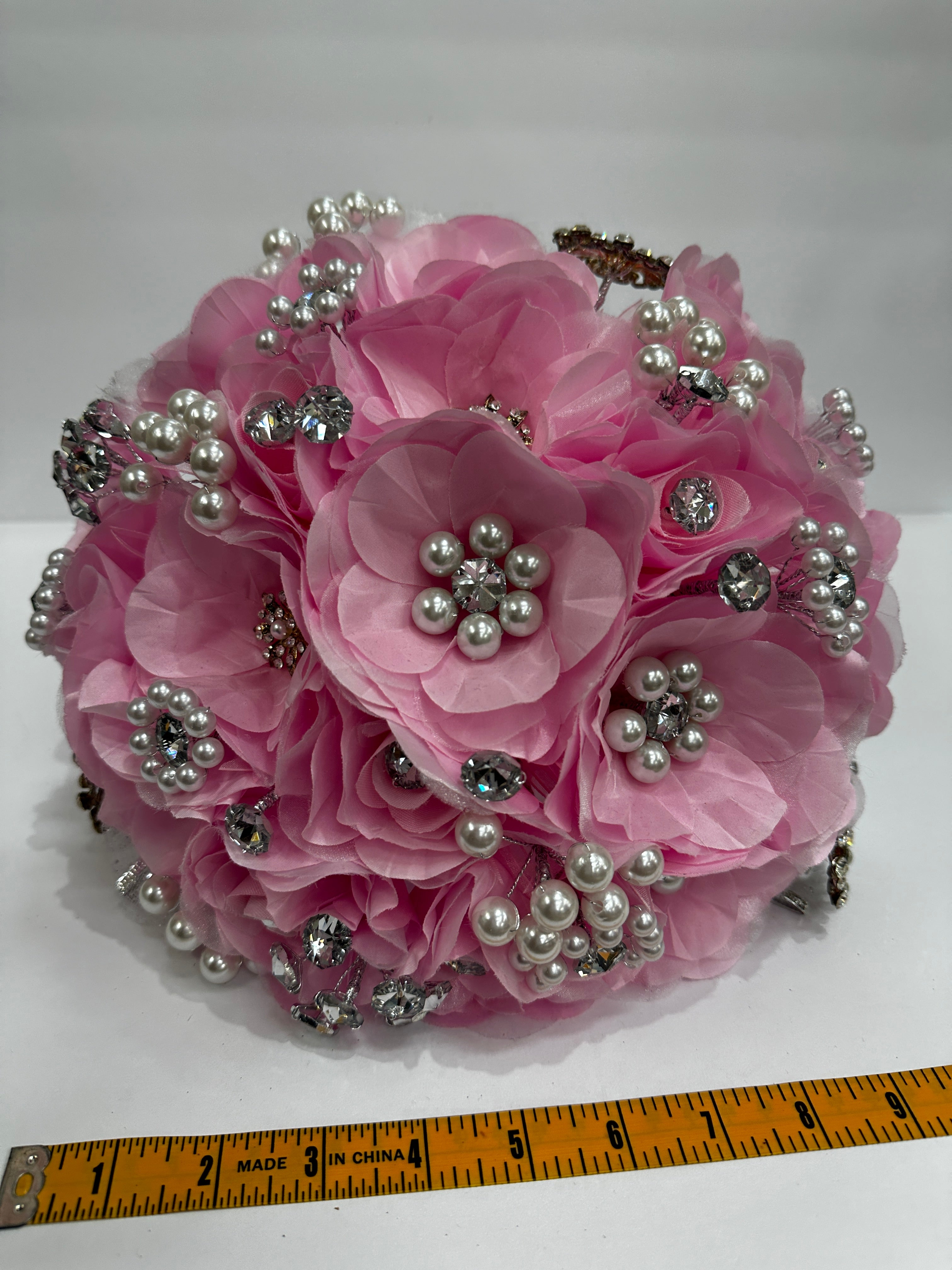 Pink floral bouquet with decorative silver application  and pearls on a white background with a ruler for scale about 9 inches length.