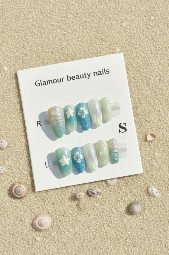 A set of decorative press-on nails displayed on a white card labeled 'Glamour beauty nails' with size markers R and S, photographed against a sand background
