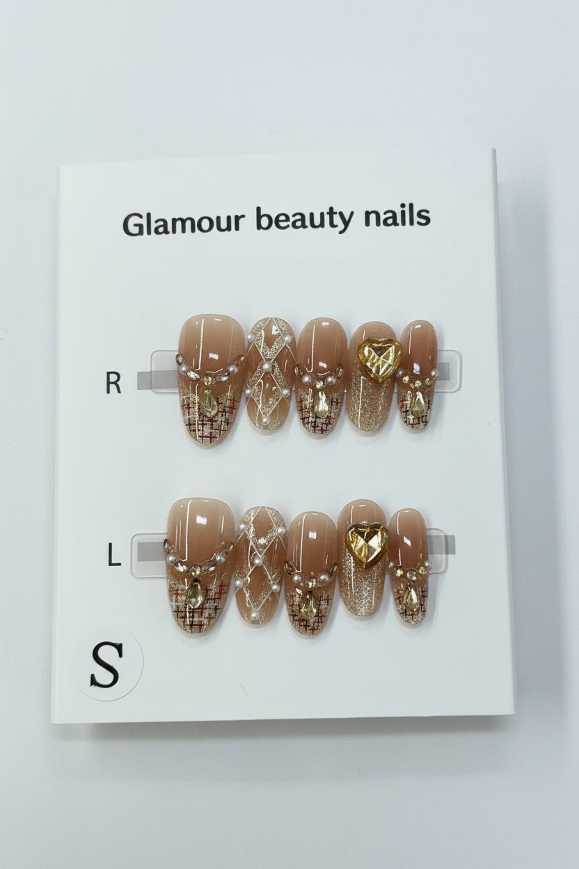 A pair of press-on nails displayed on a white card labeled 'Glamour beauty nails' with size labels R, L, and S. The nails have a nude beige base with gold glitter patterns and a central gold heart accent.