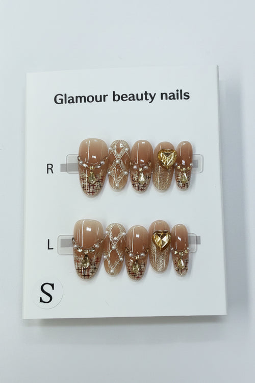 A pair of press-on nails displayed on a white card labeled 'Glamour beauty nails' with size labels R, L, and S. The nails have a nude beige base with gold glitter patterns and a central gold heart accent.