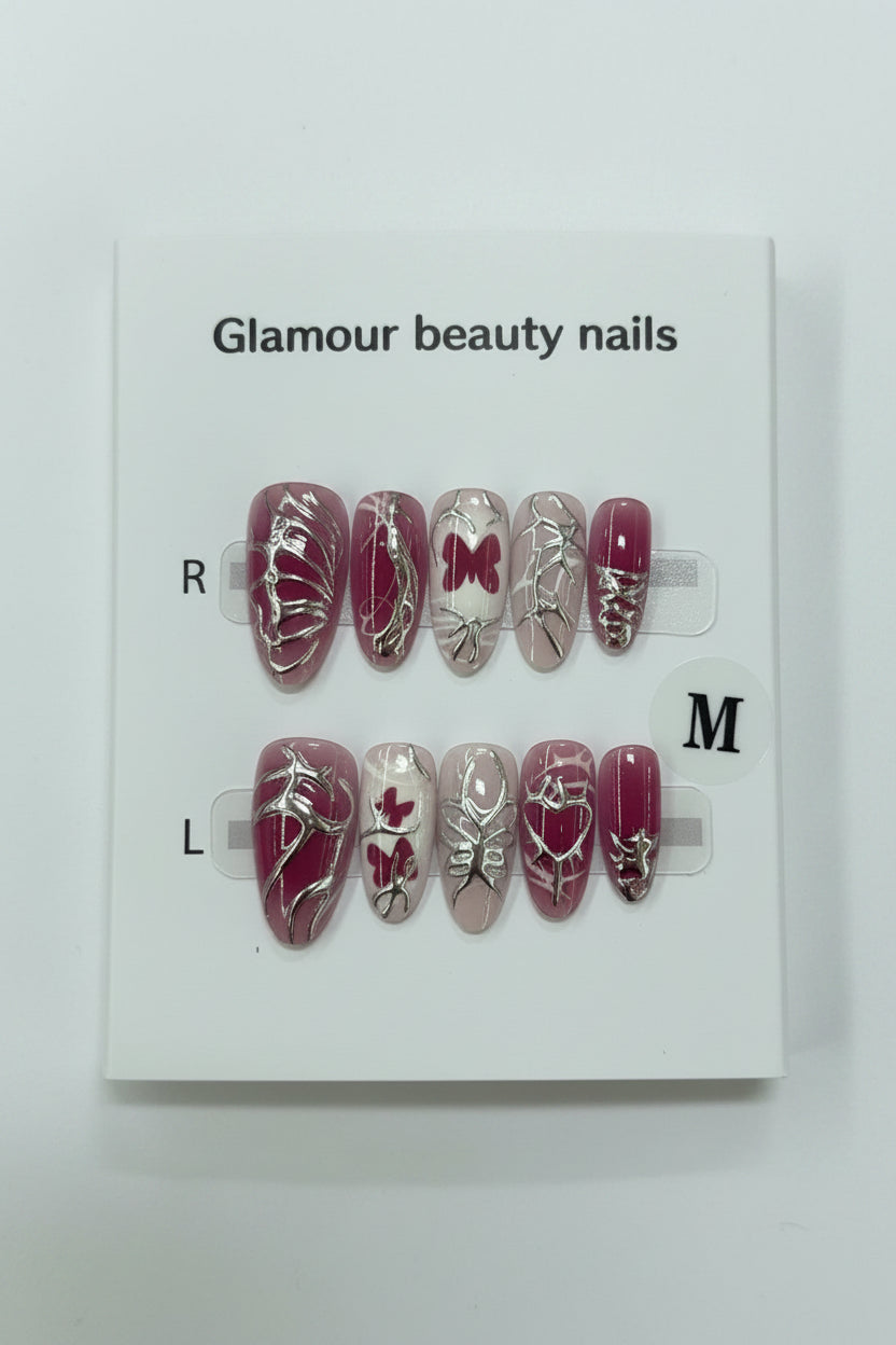 A pair of false press-on nails displayed on a white card labeled 'Glamour beauty nails' with size marker M  The nails feature a deep pink base with silver glitter patterns, including butterflies, hearts, and abstract designs.